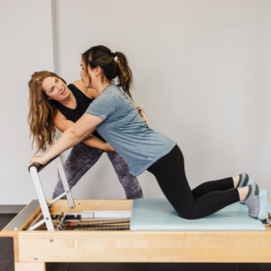Physical therapist guiding a patient through core and hip strength exercises on a Pilates reformer.