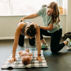 Pelvic floor therapist guiding a patient through a deep core engagement exercise, with her baby present to support the workout.