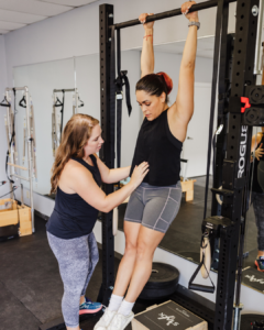 Pelvic floor therapist guiding a client with diastasis recti on proper core engagement during pull-ups.