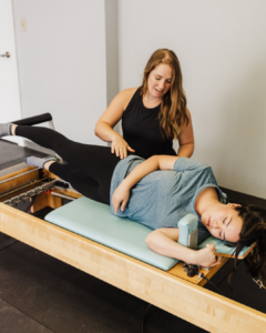 A pelvic floor physical therapist guiding a post-op tummy tuck patient through gentle core strengthening exercises on a Pilates reformer.