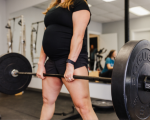 A pregnant patient lifts weights while her pelvic floor therapist monitors her form, ensuring she is lifting safely with proper support.