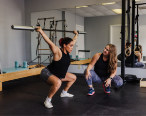A pelvic floor therapist guides a patient through a lifting exercise, ensuring proper form and core engagement. The patient is focused, practicing technique under supervision.